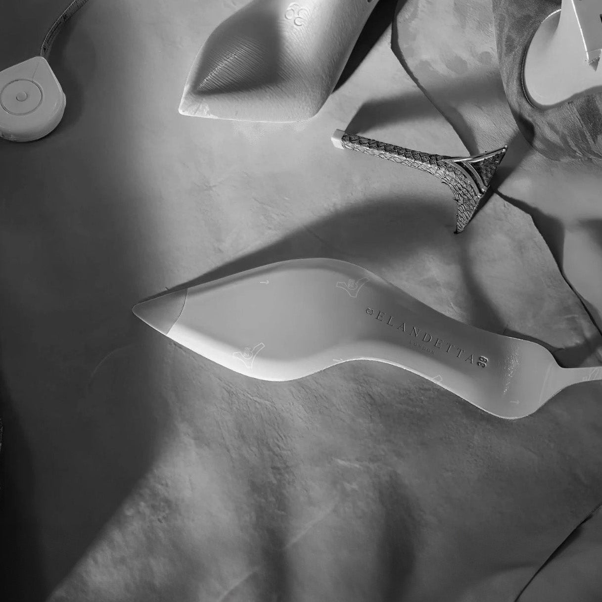 Monochrome view of Elandetta luxury heel components, including a shoe sole embossed with the brand name and leather cut‑outs used in the handcrafted production process, highlighting the craftsmanship behind the collection.