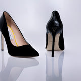 A pair of black high-heeled pumps by Elandetta, shown from the front and back on a reflective white surface. The front shoe features a matte black suede leather, while the back shoe displays a glossy black textured finish with a gold V logo on the heel and a beige insole.