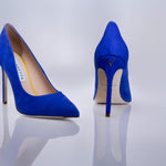 A pair of bright blue pointed-toe high heels with a textured sea leather, shown from the front and back on a reflective light gray studio surface. The brand name logo is visible on the insole.