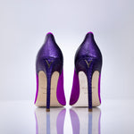 A pair of magenta textured stiletto heels shown from the back on a reflective white surface against a light gray background.