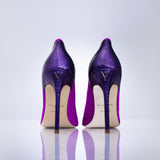 A pair of magenta textured stiletto heels shown from the back on a reflective white surface against a light gray background.