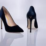 A pair of pointed-toe high heels in dark navy blue textured suede leather, shown from both the side and back angles on a reflective white surface.