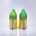 A pair of high-heeled stiletto pumps shown from the back, featuring a vibrant green and yellow python-patterned upper and a bright yellow heel counter, with a beige insole and a small gold ogo on the back.