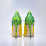 A pair of high-heeled stiletto pumps shown from the back, featuring a vibrant green and yellow python-patterned upper and a bright yellow heel counter, with a beige insole and a small gold ogo on the back.