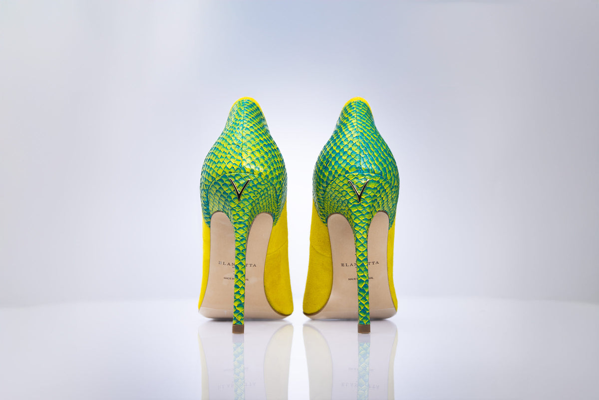 A pair of high-heeled stiletto pumps shown from the back, featuring a vibrant green and yellow python-patterned upper and a bright yellow heel counter, with a beige insole and a small gold ogo on the back.