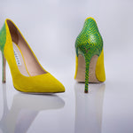 A pair of pointed-toe high heels by Versace, featuring a bright yellow suede-like body and a green snakeskin-patterned upper and heel, displayed on a reflective light gray surface.